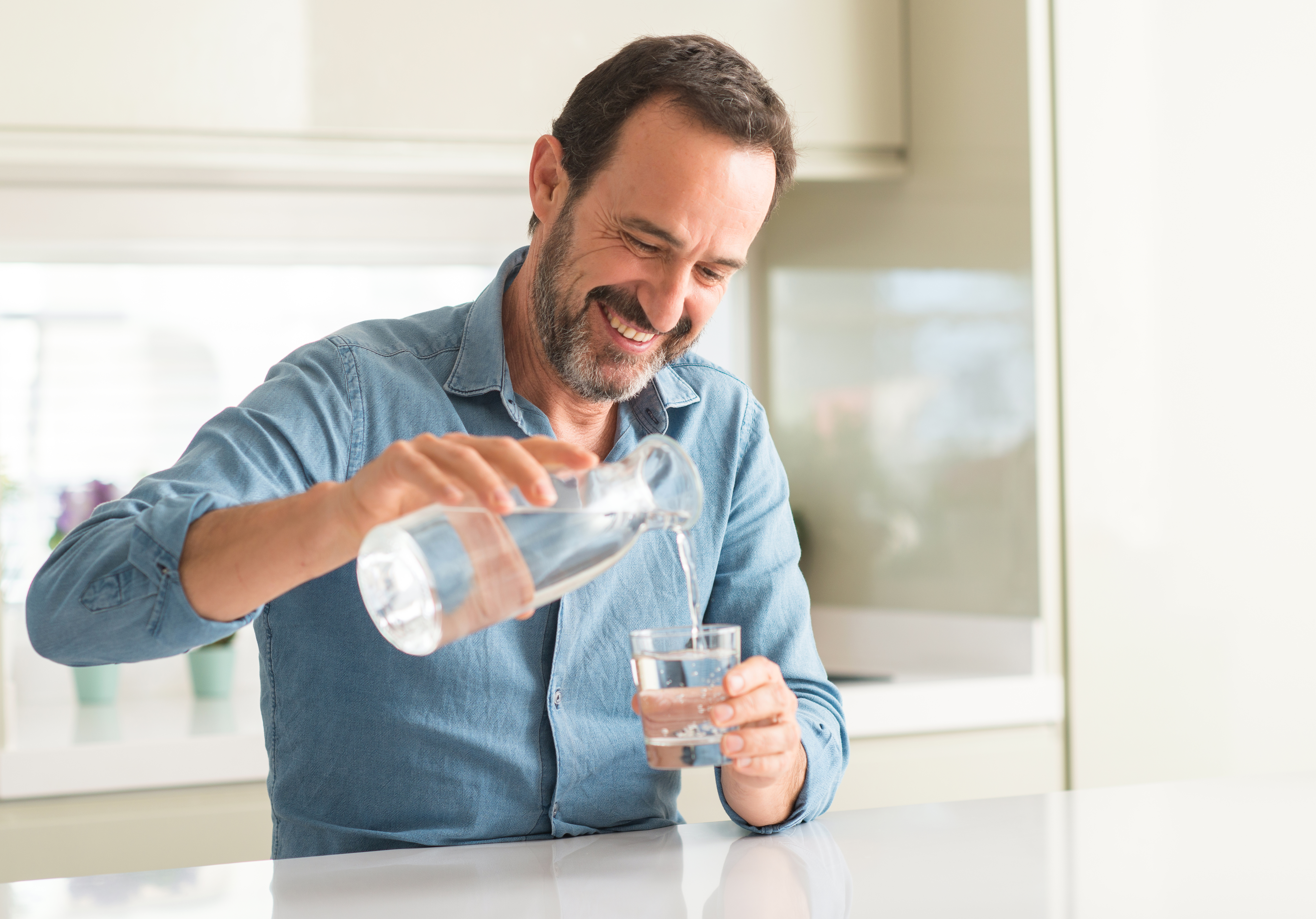 Personne d'âge moyen souriant car il se verse un verre d'eau