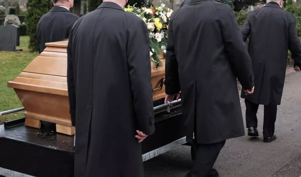 4 personnes portent un cercueil pendant un enterrement