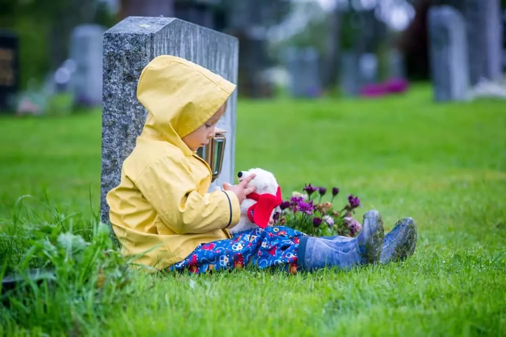 un enfant fais le deuil à coté d'une tombe suite à la perte d'un parent